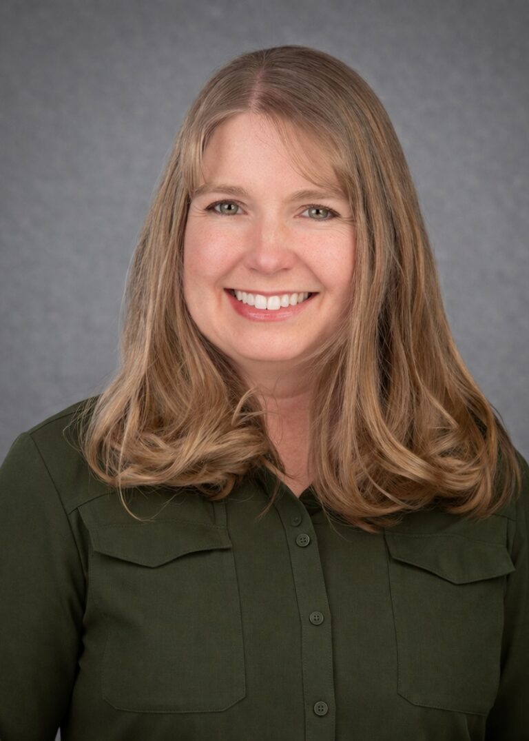 Headshot of Brittany Garwood, smiling with long light brown hair and a dark green blouse against a gray studio background