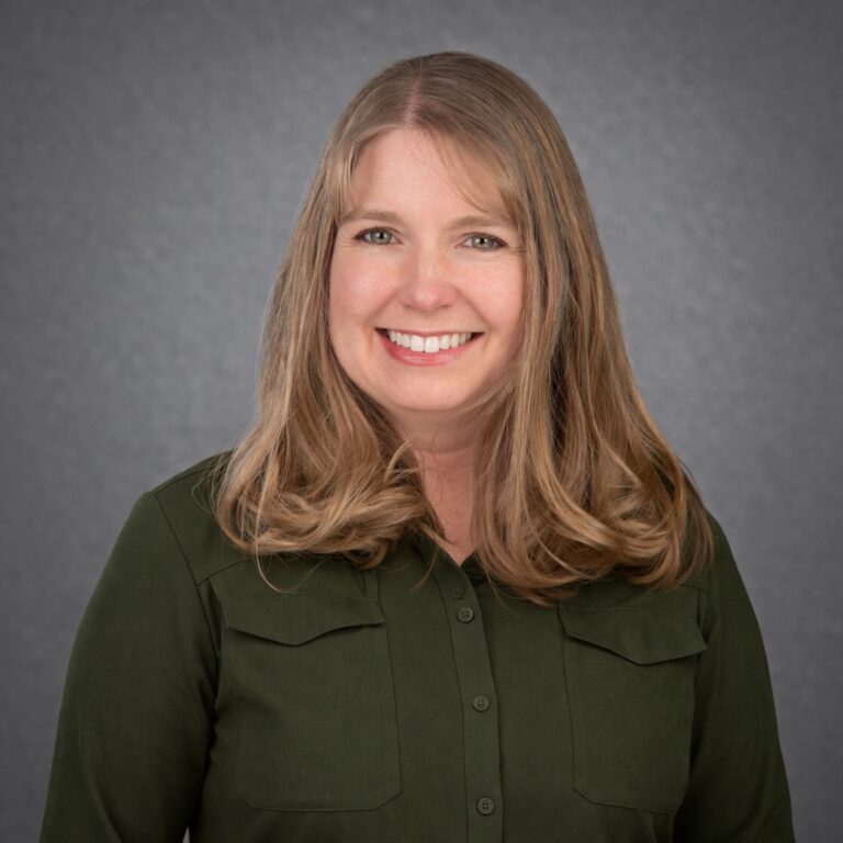 Headshot of Brittany Garwood, smiling with long light brown hair and a dark green blouse against a gray studio background