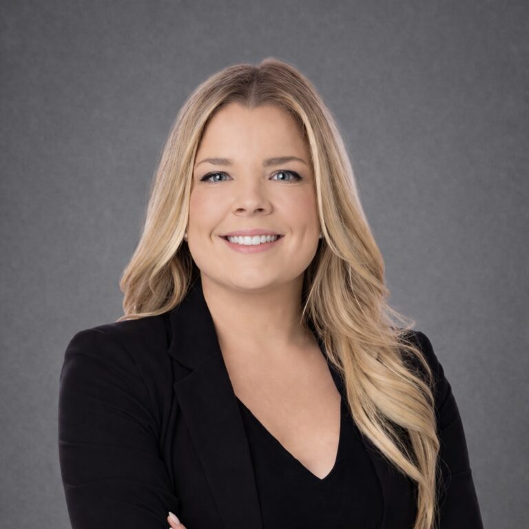 Headshot of Megan Coleman, smiling with arms crossed in a black blazer against a gray studio background.