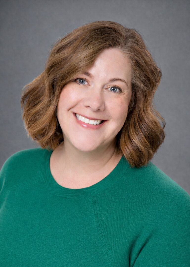 Headshot of Mindy Walker smiling in a green sweater against a gray studio background