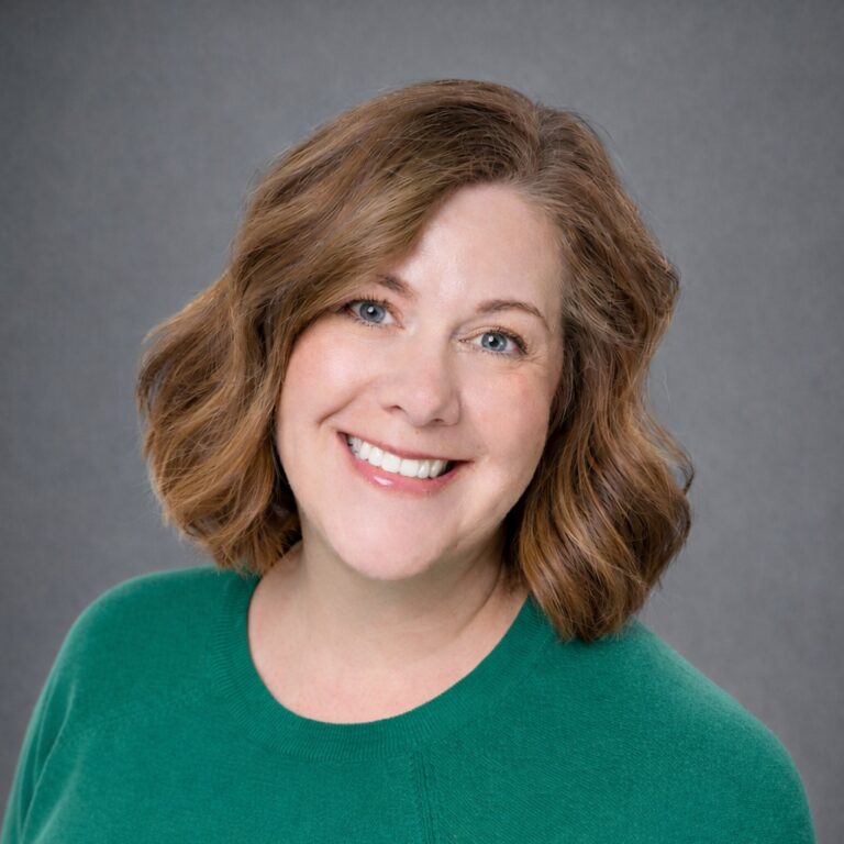 Headshot of Mindy Walker smiling in a green sweater against a gray studio background