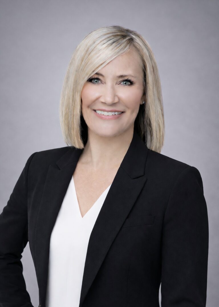 Headshot of Tami Greene, smiling with shoulder-length blonde hair, wearing a black blazer over a white blouse.