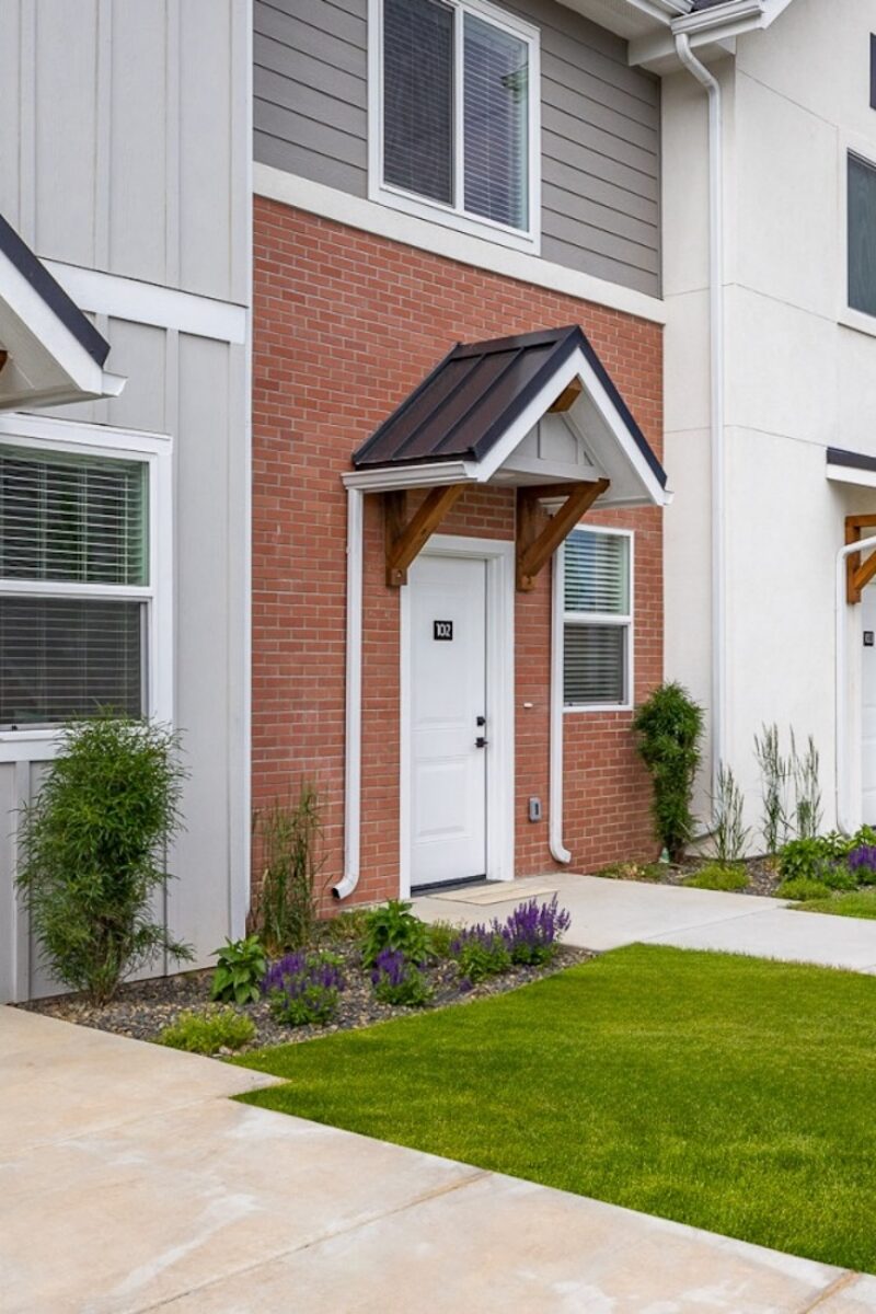Row of modern townhomes with small covered entries, white doors, brick accents, and landscaped walkways.