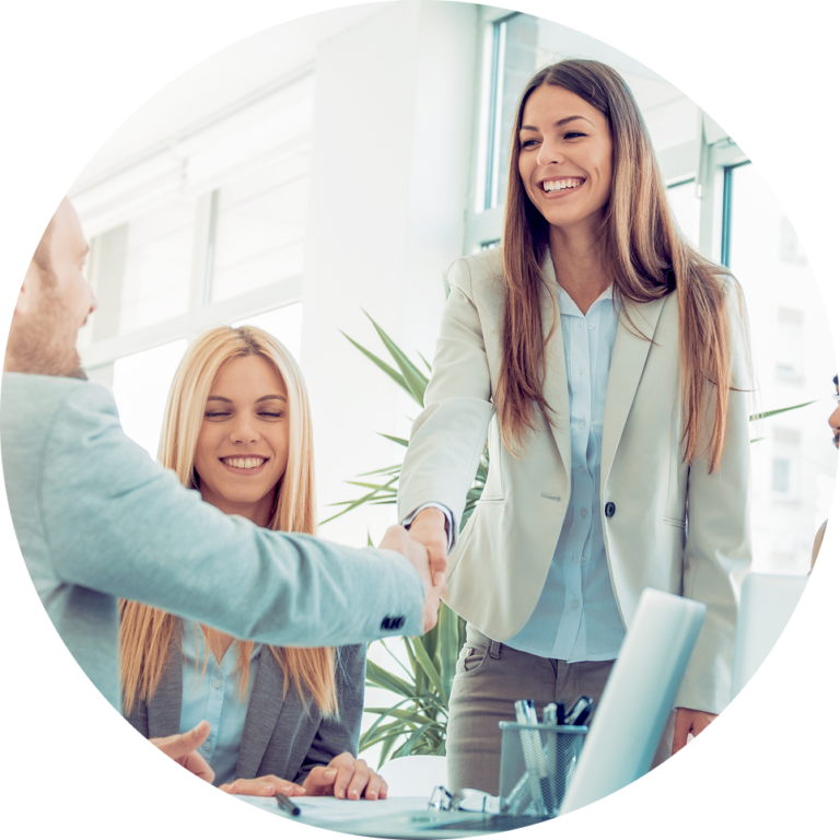 Smiling businesswoman shaking hands with a colleague in a bright office while coworkers sit at the table