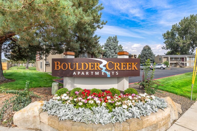 Boulder Creek Apartments sign in a landscaped flower bed beside the apartment complex and parking lot