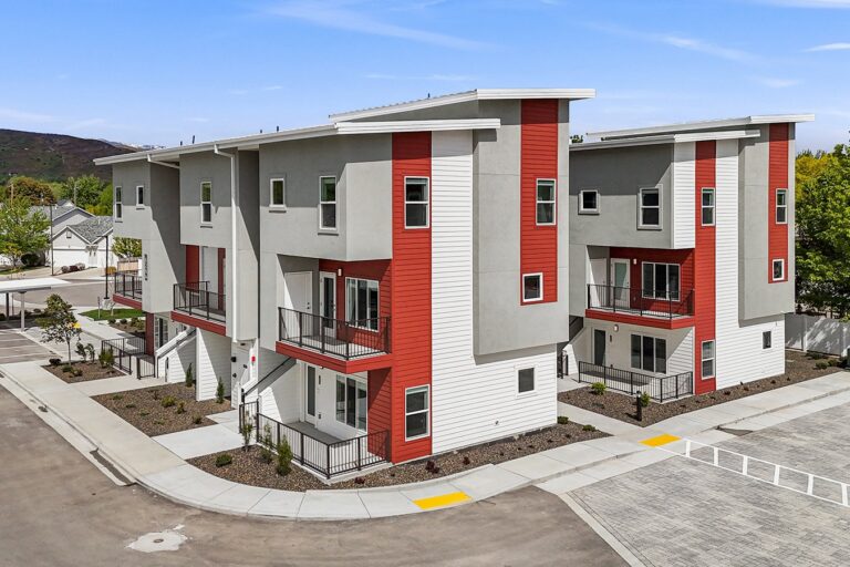 Modern three-story apartment buildings with gray, white, and red siding, balconies, and landscaped walkways.