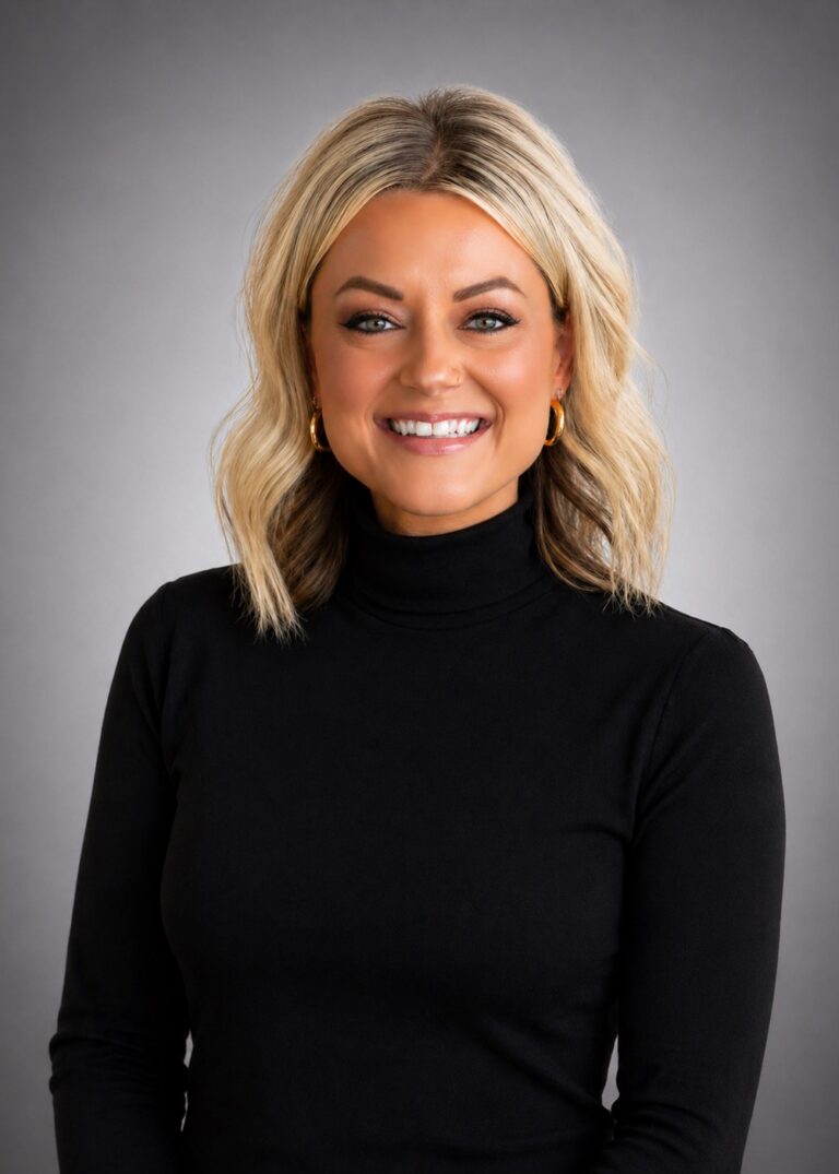 Smiling woman with shoulder-length blonde hair, gold hoop earrings, and a black turtleneck against a gray studio background