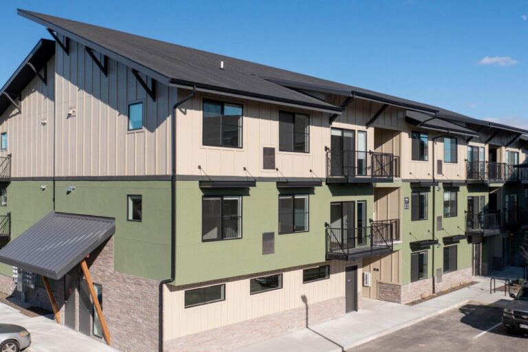 Modern three-story apartment building with green and beige siding, black roof, and small balconies.