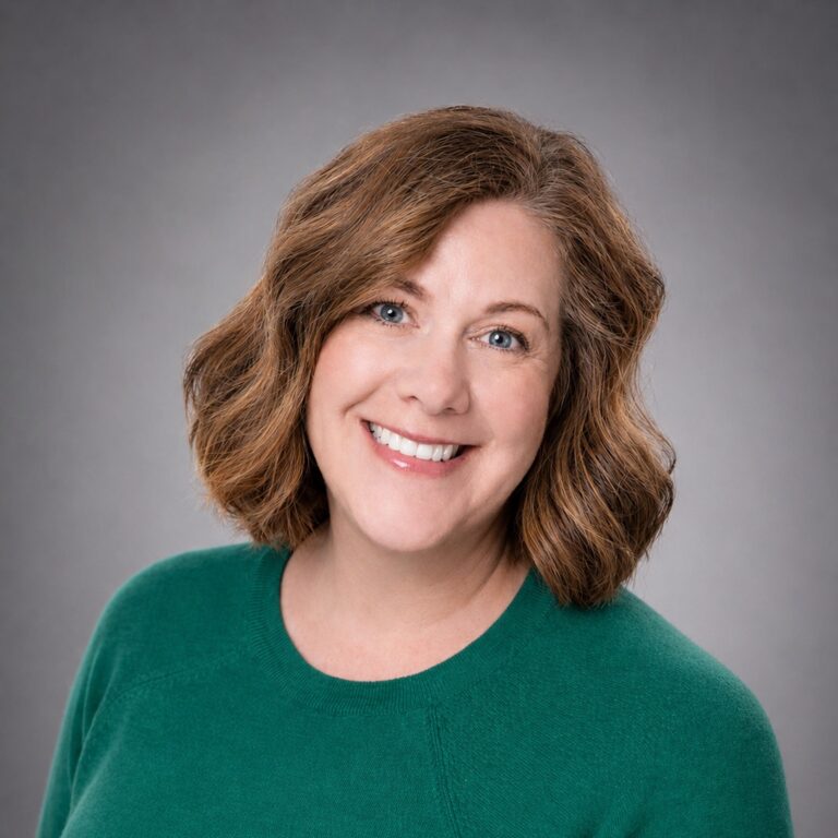 Smiling woman with shoulder-length wavy brown hair in a green sweater against a gray studio background