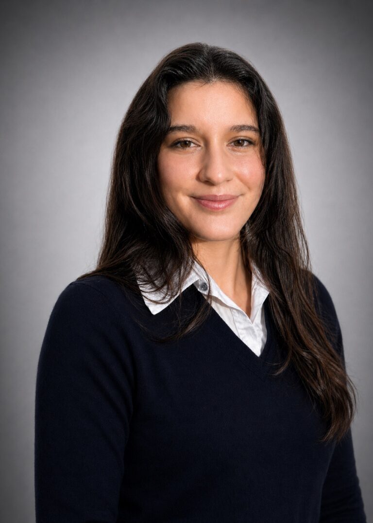 Professional headshot of a woman with long dark hair, wearing a navy sweater over a white collared shirt.