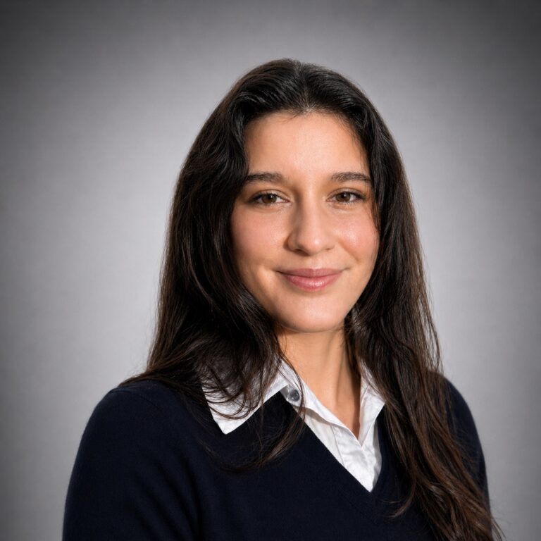 Professional headshot of a woman with long dark hair, wearing a navy sweater over a white collared shirt.